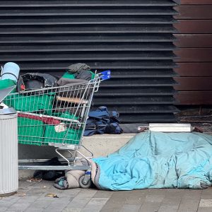 Shopping trolley with belongings and bedding on a footpath in front of a roller door