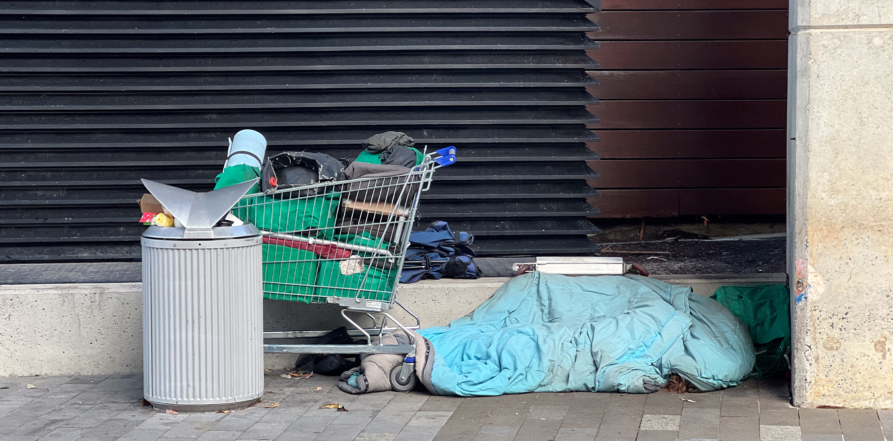 Shopping trolley with belongings and bedding on a footpath in front of a roller door
